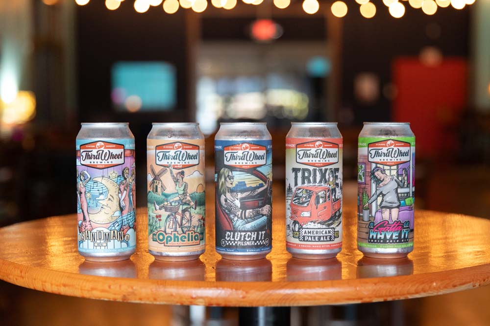 Third Wheel Beer cans on table with twinkly lights in background